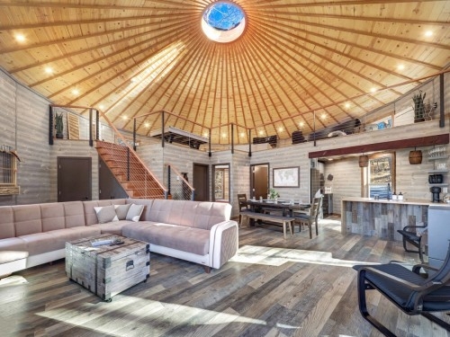 Spacious, modern cabin-like yurt featuring a wooden interior with a glowing central skylight and a loft overlooking a cozy living space, complete with contemporary amenities for comfort and convenience